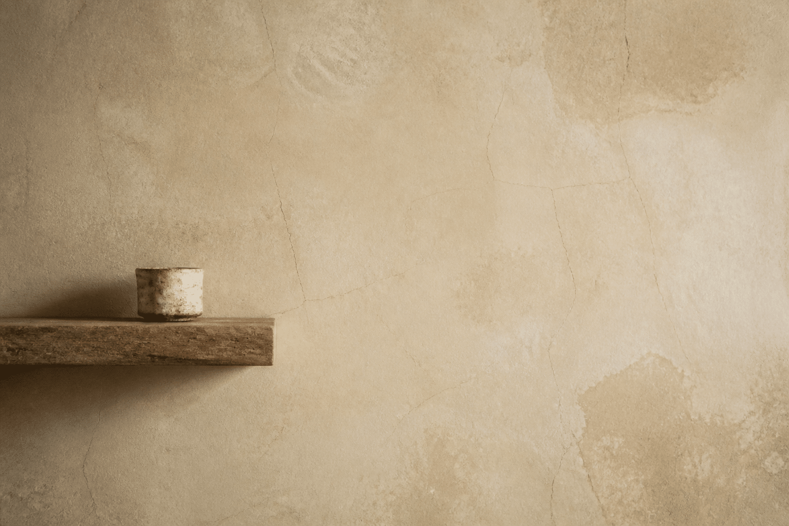 Mur en chaux patiné de couleur beige avec texture irrégulière, étagère en bois et tasse en céramique